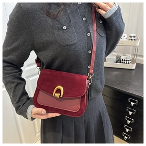Detail of burgundy shoulder bag featuring a gold horseshoe buckle and suede panel
