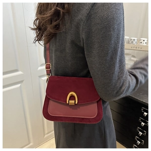 Detail of vintage burgundy saddle bag with suede flap and gold arch buckle on a model