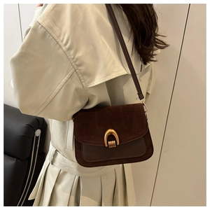 Detail view of brown suede saddle bag with gold horseshoe buckle on beige trench coat