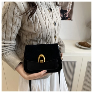 Close-up of a black suede saddle bag with a golden horseshoe buckle in a lifestyle setting