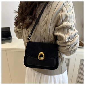 Detail of black crossbody bag with gold horseshoe buckle on beige sweater