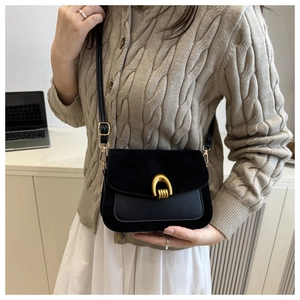 Detail view of black textured leather bag featuring a gold horseshoe buckle on beige knitwear