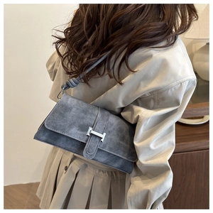 Detalle de bolso bandolera de ante gris con hebilla en H de plata usado al hombro
