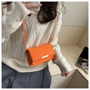 Détail du petit sac à bandoulière orange avec motif crocodile et boucle dorée sur modèle