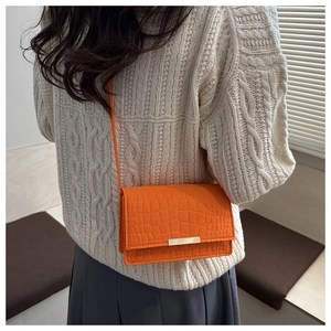 Détail du sac bandoulière orange vif avec texture crocodile et boucle en métal doré