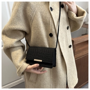 Gros plan du sac bandoulière noir motif crocodile avec boucle dorée sur un manteau beige