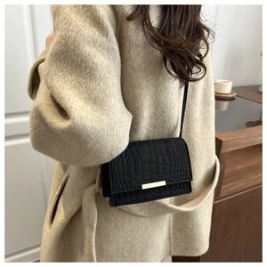 Détail d'un sac à bandoulière noir motif crocodile avec fermoir en métal doré porté par un modèle