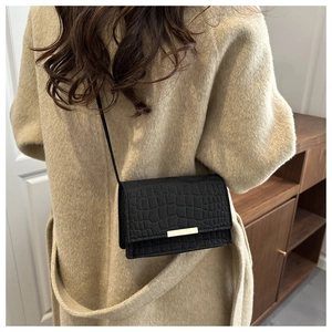 Détail d'un sac bandoulière noir motif crocodile avec boucle métallique dorée rectangulaire