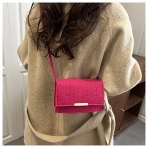 Détail du petit sac bandoulière rose fuchsia à motif croco sur un manteau beige