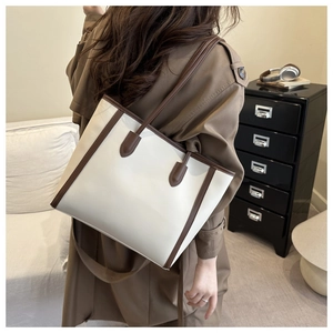 Detail view of a vintage cream leather tote bag with brown straps worn by a model in a room