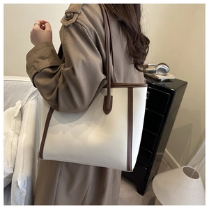 Detail view of cream and brown contrast tote bag worn over the shoulder in a cozy room