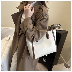 Detail of minimalist cream and brown leather tote bag worn with a long trench coat