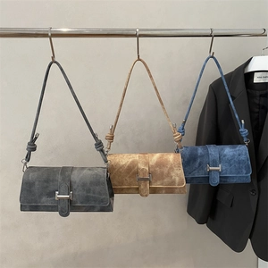 Tres bolsos de hombro minimalistas en ante azul y caramelo colgados en un estante de exhibición