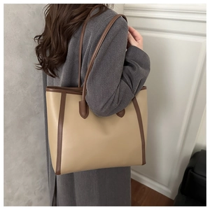 Detail of a large beige tote bag with brown trim styled on a grey coat for workwear