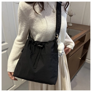 Detail of black nylon drawstring bag featuring a soft white plush doll charm accessory
