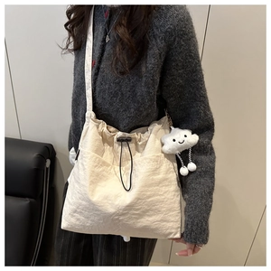 Detail of off-white tote bag featuring drawstring closure and soft cloud plush pendant