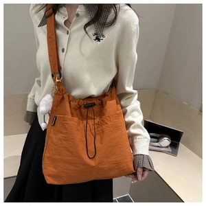 Detail of orange nylon tote bag with drawstring closure and white plush charm on model
