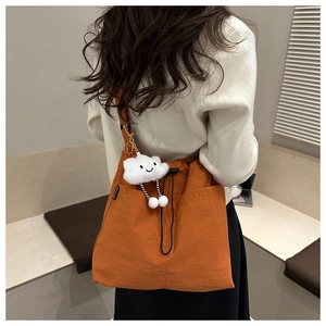 Detail of orange nylon tote bag featuring a white cloud plush charm and black drawstring