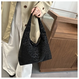 Detail of black leopard print hobo bag held by a model in a stylish trench coat