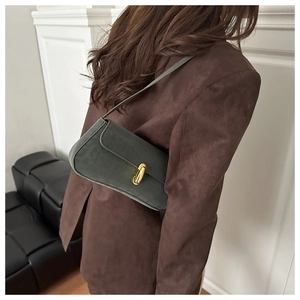 Close-up of a dark green suede baguette bag with a gold capsule buckle on a model