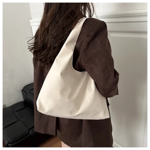 Detail of a minimalist creamy white hobo shoulder bag styled with a brown wool coat