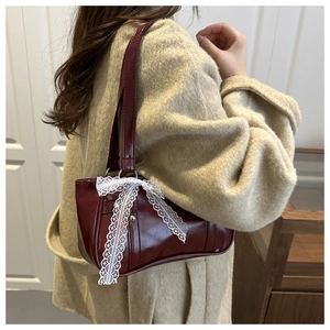Detalle de bolso burdeos con lazo de encaje blanco sobre chaqueta de tweed beige