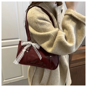 Detail of burgundy patent leather shoulder bag with white lace bow and metal studs
