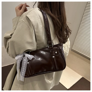 Close-up of dark brown patent leather bag with white lace bow and silver ring detail