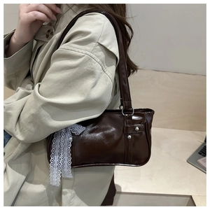 Close-up of a dark brown patent leather shoulder bag with a lace bow detail