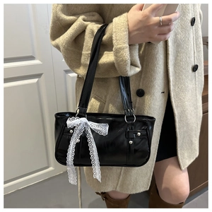 Detail of glossy black patent leather shoulder bag with white lace bow and metal rings