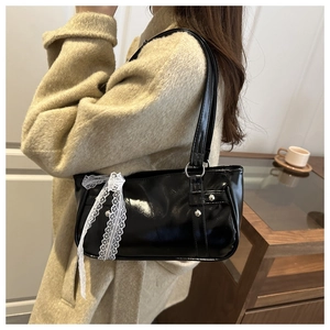 Detail of black patent leather underarm bag with silver studs and lace bows