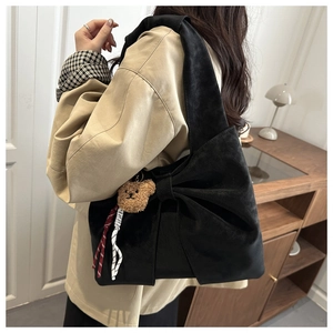 Detail of black matte shoulder bag with a large bow and a cute brown bear charm