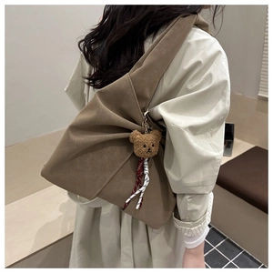 Detailed side view of a brown oversized tote bag with a plush bear charm on a model