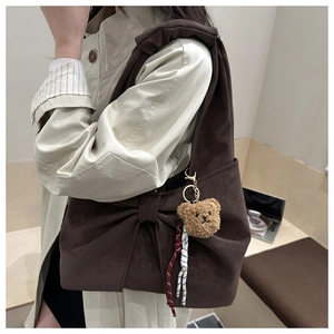 Detail of dark brown tote bag with bow, plush bear charm and woven side straps