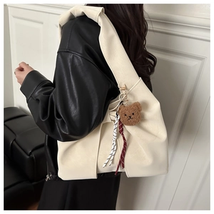 Detail of a creamy white faux leather tote bag featuring a cute brown plush bear charm