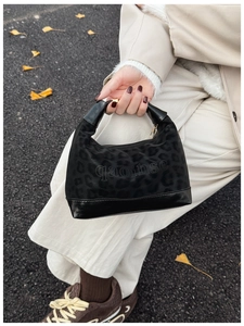 Detail of leopard print handbag with leather strap held against autumn background