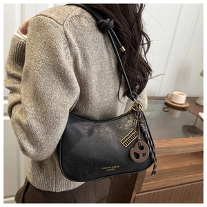 Détail d'un sac à bandoulière vintage en cuir noir plissé avec breloques bouclier dorées