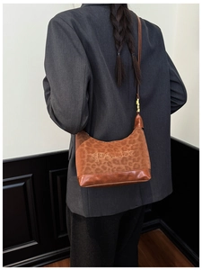 Detail of a brown leopard print shoulder bag worn by a model in a gray suit