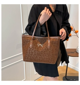 Close-up of leopard print tote bag featuring a decorative metallic bow and leather handle