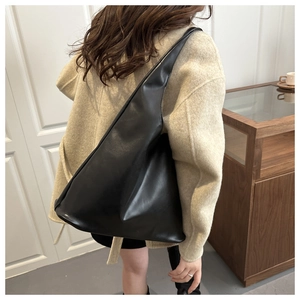 Borsa tote triangolare minimalista in pelle nera indossata da una modella in interno