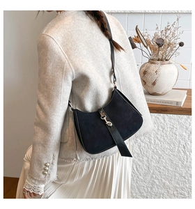 Detail of black suede hobo bag with gold piston lock worn over a tweed jacket