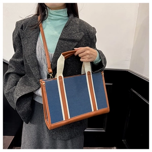 Detail of blue canvas tote bag featuring brown leather trim and white woven handles