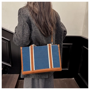 Detail of blue denim tote bag with leather trim worn on a grey tweed blazer