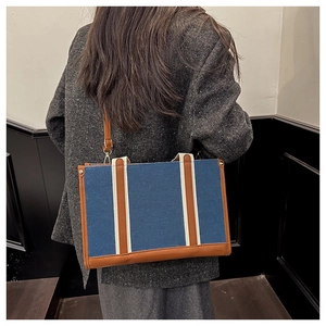 Detail of navy blue canvas tote bag with brown leather straps and silver metal rivets