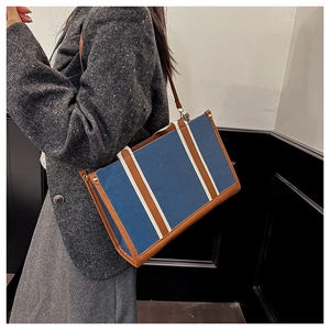 Side view of denim tote bag with leather straps on model wearing grey wool coat