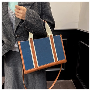 Detail of navy canvas tote with brown leather trim and striped webbing straps on model