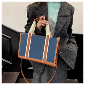 Detail of blue denim tote bag with brown leather trim and beige fabric handles