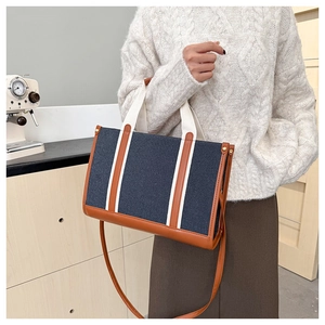 Detail of canvas tote bag with brown leather bottom and golden metal rivet accents