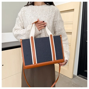 Detailed view of navy canvas tote bag with brown leather trim and beige woven handles