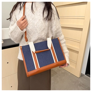 Detail of blue denim tote bag with brown leather handles and cream textile straps